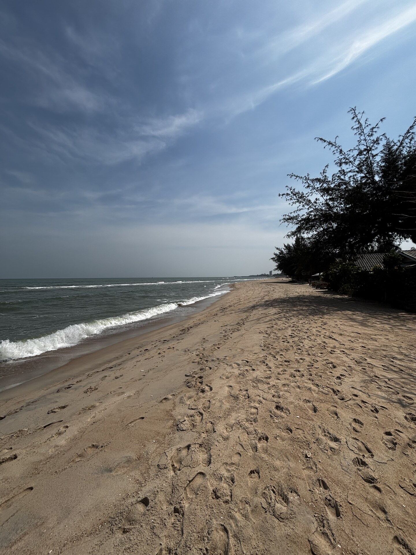 Cha-Am beach in Thailand on a sunny day with waves rolling in onto empty sand