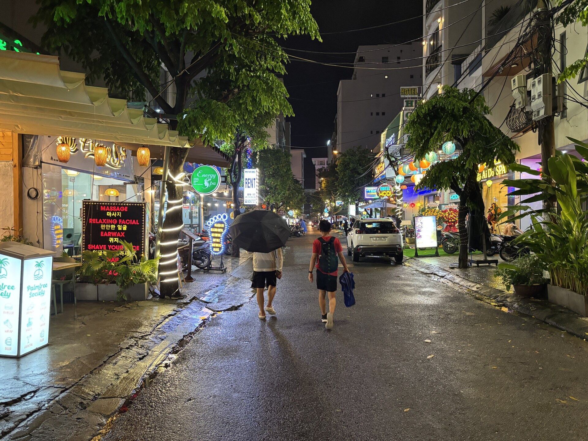 A wet street in Da Nang at night with people walking under umbrellas during October monsoon rain