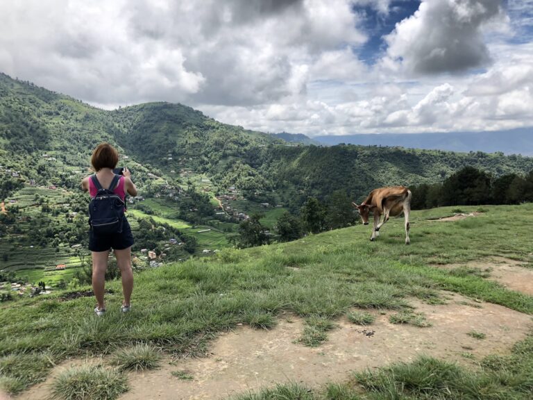 A trekker on a green hillside above a terraced Nepali village on the Mardi Himal trail